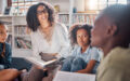 Storytelling, teacher or students with talking in a library asking questions for learning development. Education, kids or children listening to a black woman speaking on fun books at school classroom